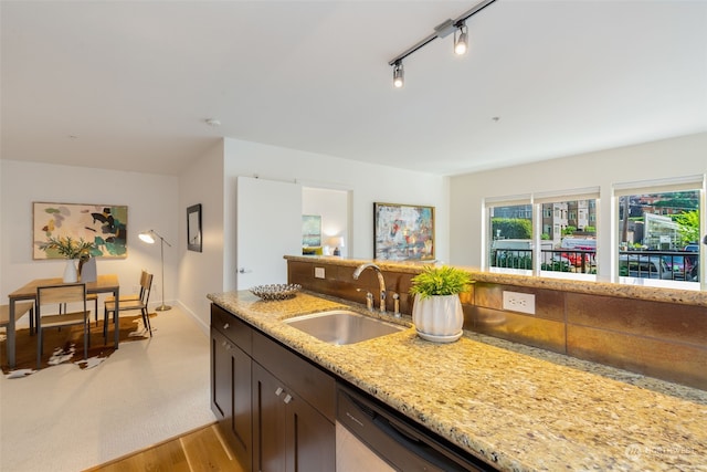 kitchen with light stone countertops, dishwasher, sink, dark brown cabinetry, and light hardwood / wood-style flooring