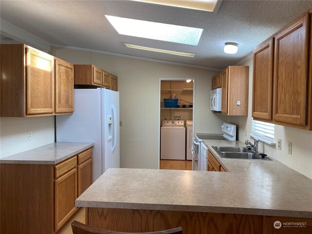 kitchen with vaulted ceiling with skylight, sink, washing machine and clothes dryer, kitchen peninsula, and white appliances