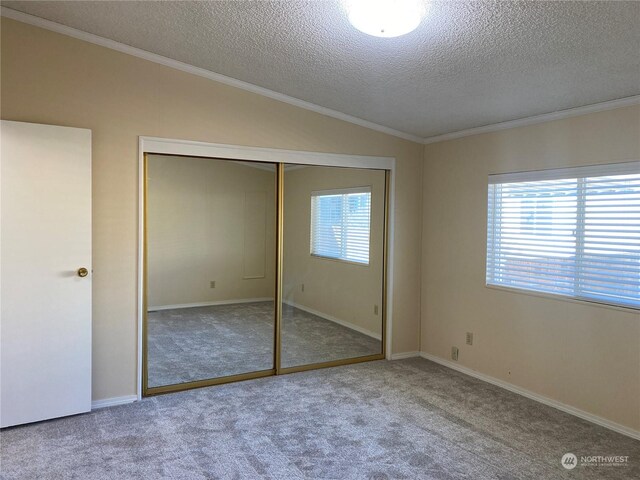 unfurnished bedroom with crown molding, carpet, a textured ceiling, vaulted ceiling, and a closet