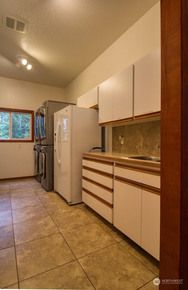 kitchen with stacked washer and dryer, white cabinetry, white fridge with ice dispenser, and light tile patterned flooring