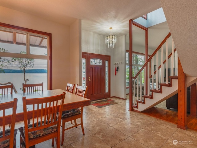 entryway with light tile patterned floors, a textured ceiling, a chandelier, and a water view