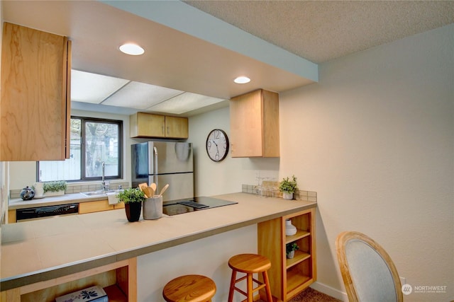 kitchen featuring a breakfast bar, light brown cabinetry, black appliances, sink, and kitchen peninsula