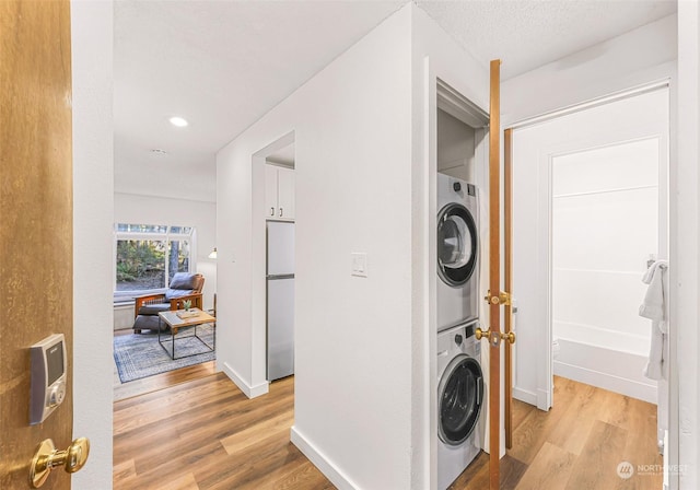 laundry area with stacked washer and dryer, light hardwood / wood-style floors, and a textured ceiling