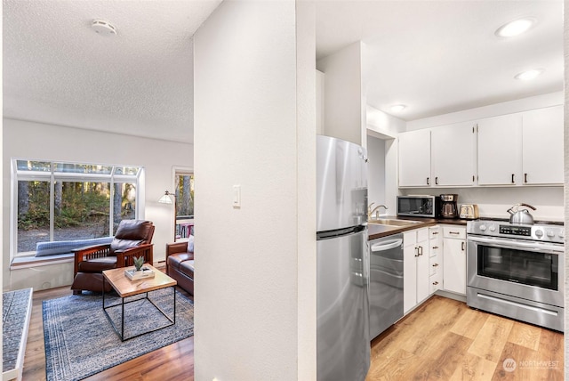 kitchen featuring sink, white cabinetry, stainless steel appliances, a textured ceiling, and light wood-type flooring