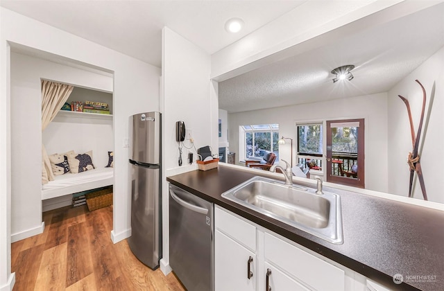 kitchen featuring sink, appliances with stainless steel finishes, light hardwood / wood-style floors, a textured ceiling, and white cabinets