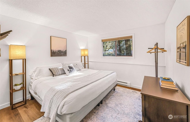 bedroom with hardwood / wood-style flooring, a textured ceiling, and a baseboard heating unit