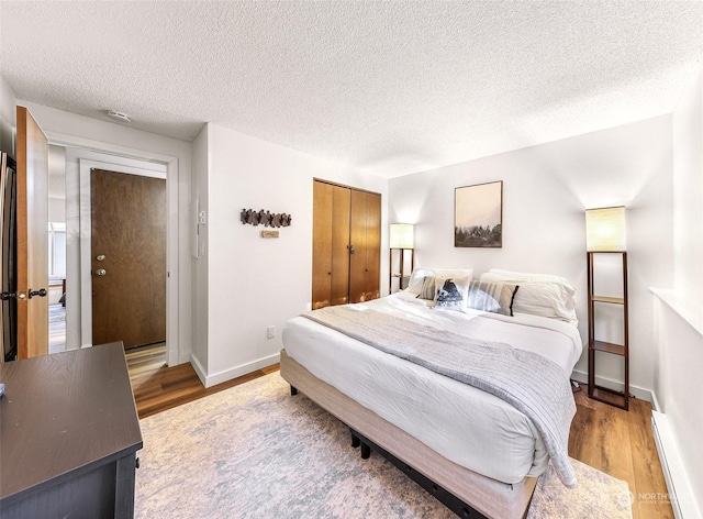 bedroom featuring hardwood / wood-style flooring, a textured ceiling, a closet, and a baseboard heating unit