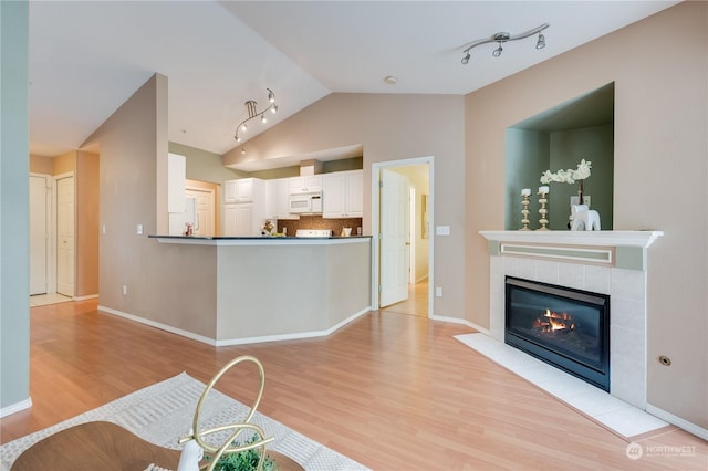 living room featuring lofted ceiling, a tile fireplace, baseboards, light wood-style floors, and rail lighting