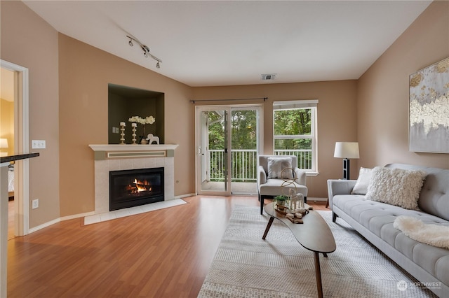 living room featuring a tiled fireplace, light hardwood / wood-style floors, vaulted ceiling, and track lighting