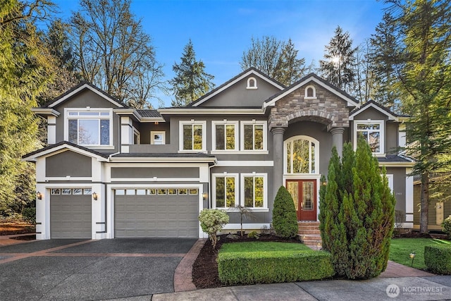 view of front of home with driveway, stone siding, an attached garage, and stucco siding