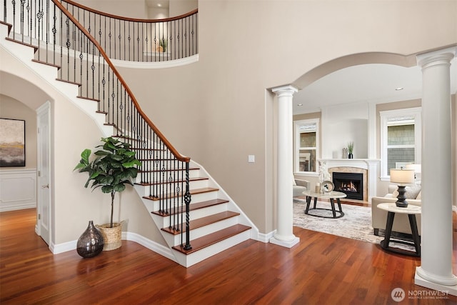 stairs with a fireplace, decorative columns, a high ceiling, and wood finished floors