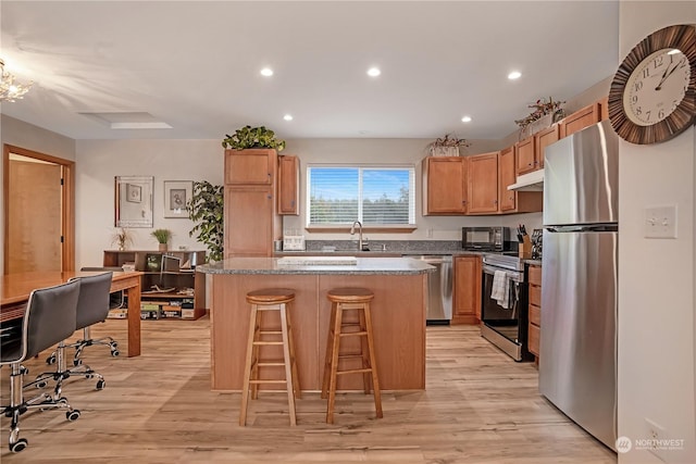 kitchen with appliances with stainless steel finishes, a breakfast bar, a kitchen island, and light wood-type flooring