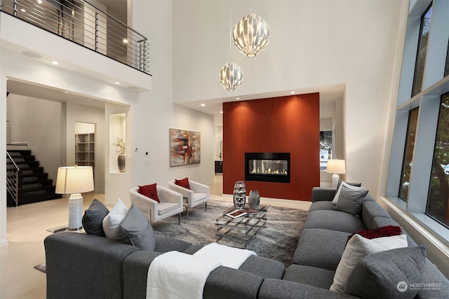 living room featuring a glass covered fireplace, a towering ceiling, stairway, a notable chandelier, and recessed lighting