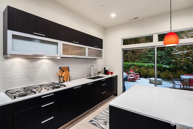 kitchen with dark cabinets, stainless steel gas cooktop, visible vents, and a sink