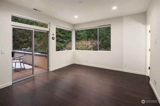unfurnished room with a wealth of natural light, wood-type flooring, visible vents, and baseboards