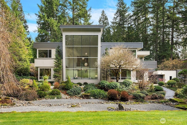 contemporary house with a front lawn, a balcony, and stucco siding