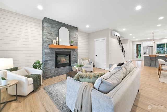 living room featuring wooden walls, a stone fireplace, light hardwood / wood-style flooring, and an AC wall unit