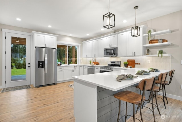 kitchen featuring a kitchen bar, white cabinetry, hanging light fixtures, appliances with stainless steel finishes, and backsplash