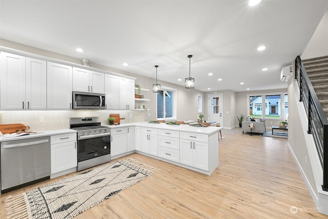 kitchen featuring a wall mounted air conditioner, decorative light fixtures, light wood-type flooring, kitchen peninsula, and stainless steel appliances