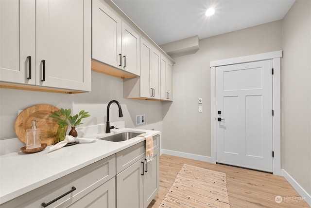 laundry area with sink, electric dryer hookup, hookup for a washing machine, cabinets, and light wood-type flooring