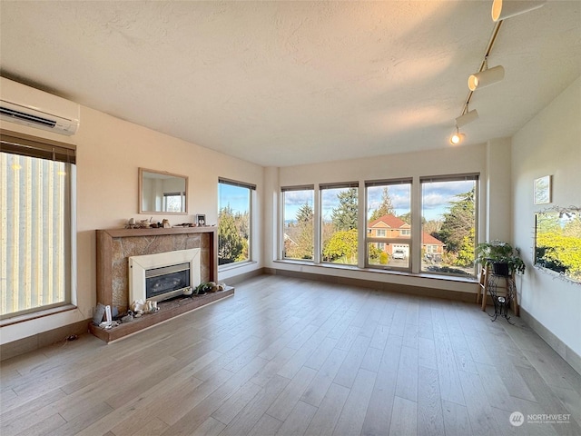 unfurnished living room featuring a premium fireplace, an AC wall unit, a textured ceiling, and light wood-type flooring