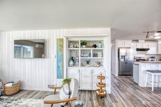 interior space featuring appliances with stainless steel finishes, hardwood / wood-style floors, wooden walls, white cabinets, and a kitchen bar