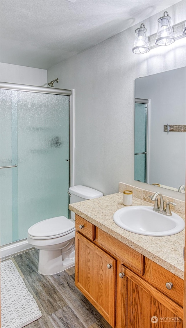 bathroom with vanity, hardwood / wood-style floors, a shower with shower door, and toilet