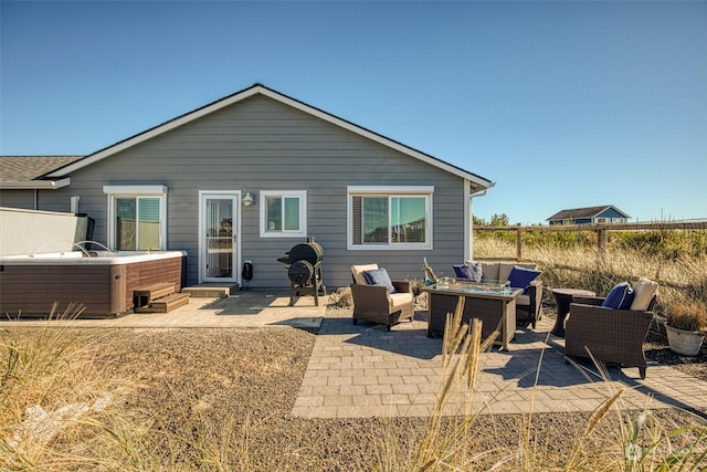 rear view of property with a hot tub, a patio, and an outdoor living space with a fire pit