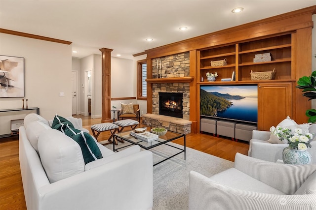 living room with crown molding, light hardwood / wood-style floors, a stone fireplace, and ornate columns