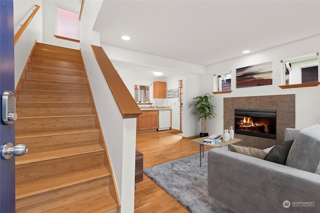 living room featuring a tiled fireplace, sink, and light hardwood / wood-style flooring