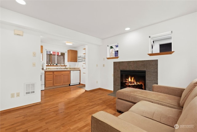 living room featuring sink, a tile fireplace, and light wood-type flooring