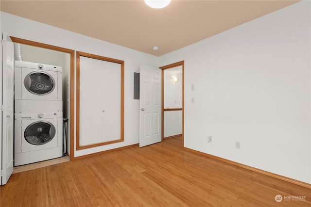 laundry room featuring stacked washer and dryer, electric panel, and light hardwood / wood-style flooring