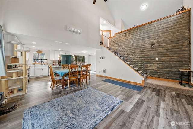 dining area with high vaulted ceiling, a wall unit AC, and light wood-type flooring