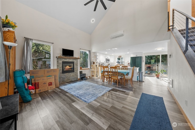 living room featuring a wall mounted air conditioner, a fireplace, high vaulted ceiling, ceiling fan, and light hardwood / wood-style floors