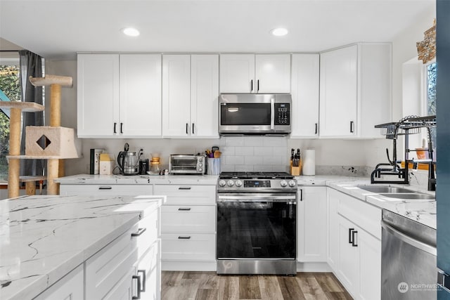 kitchen with sink, appliances with stainless steel finishes, dark hardwood / wood-style flooring, light stone countertops, and white cabinets