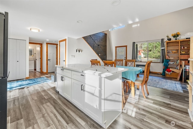 kitchen featuring white cabinetry, light hardwood / wood-style flooring, light stone countertops, and a kitchen island