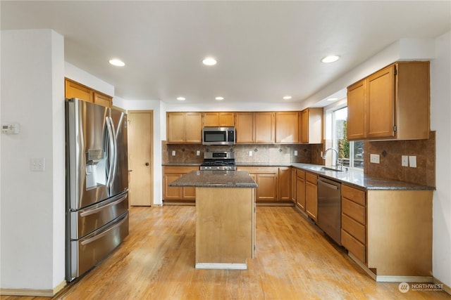 kitchen with appliances with stainless steel finishes, a center island, dark stone countertops, light hardwood / wood-style floors, and sink