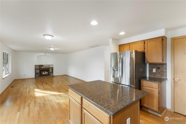 kitchen with a stone fireplace, a center island, light hardwood / wood-style floors, stainless steel fridge with ice dispenser, and backsplash