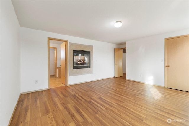 spare room featuring a multi sided fireplace and light hardwood / wood-style floors