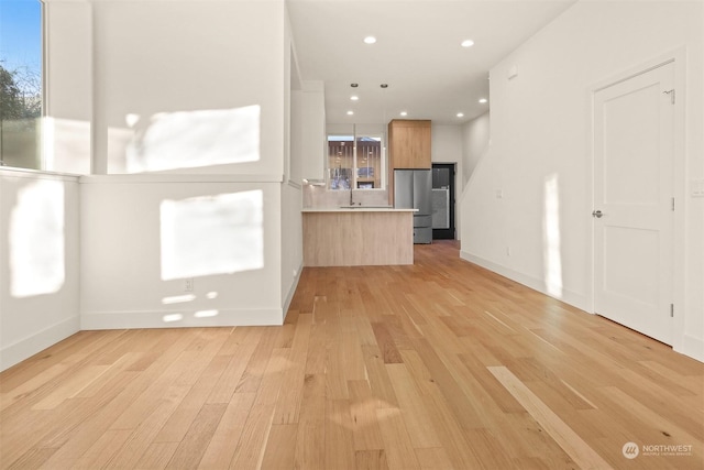 kitchen with decorative light fixtures, light hardwood / wood-style flooring, stainless steel fridge, and kitchen peninsula