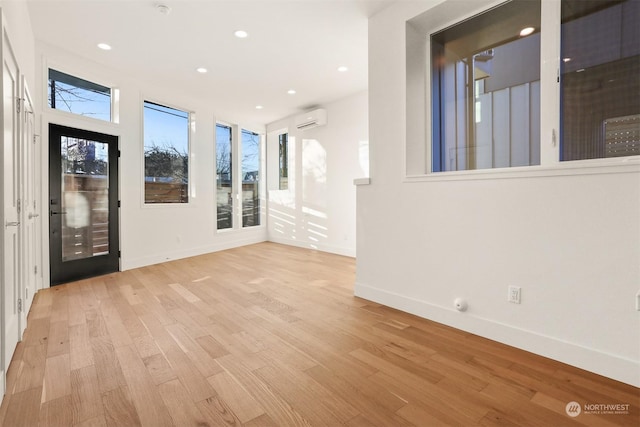 empty room featuring a wall mounted AC and light hardwood / wood-style flooring