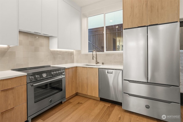 kitchen featuring sink, stainless steel appliances, tasteful backsplash, white cabinets, and light wood-type flooring