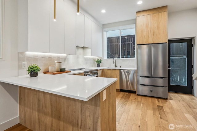 kitchen with a peninsula, light countertops, appliances with stainless steel finishes, light wood finished floors, and modern cabinets