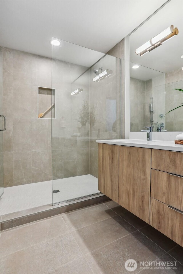 bathroom with tile patterned flooring, tiled shower, and vanity