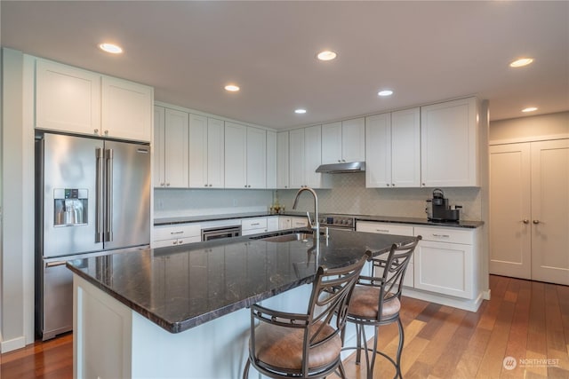 kitchen featuring white cabinets, a kitchen island with sink, sink, and stainless steel fridge