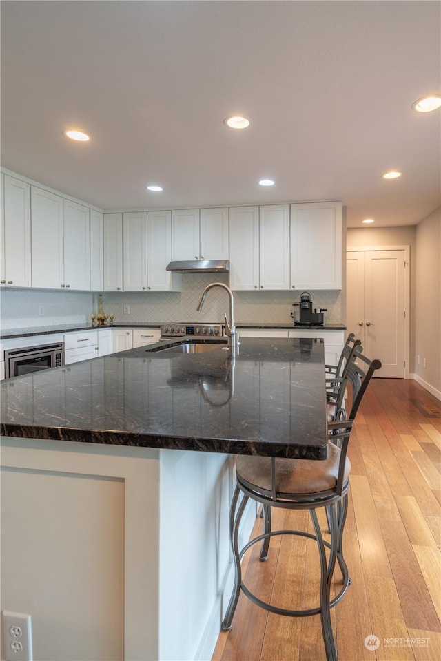 kitchen with dark stone countertops, light hardwood / wood-style floors, and white cabinets