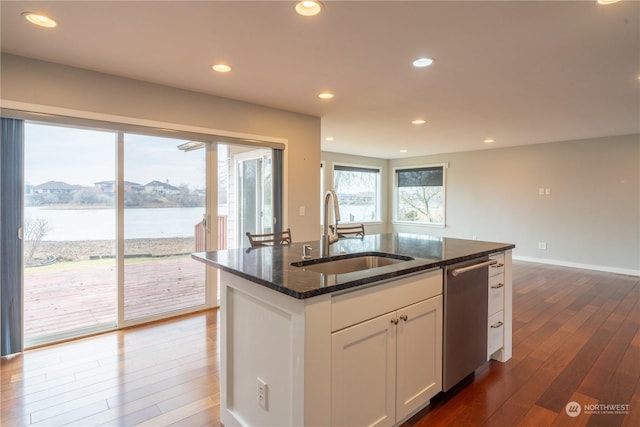 kitchen with white cabinetry, sink, dark stone counters, a kitchen island with sink, and a water view