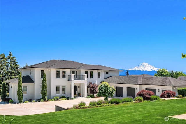 view of front of home featuring a mountain view, a garage, a balcony, and a front lawn