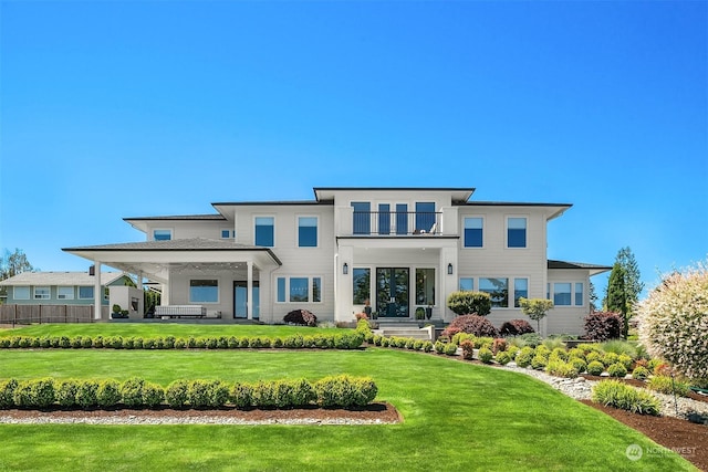 back of property with a balcony, a lawn, and a hot tub