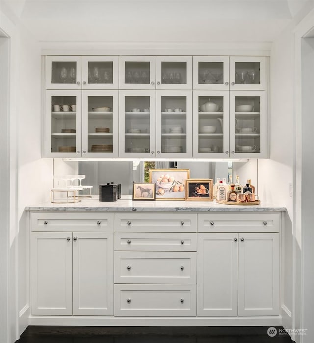 bar with light stone countertops and white cabinetry